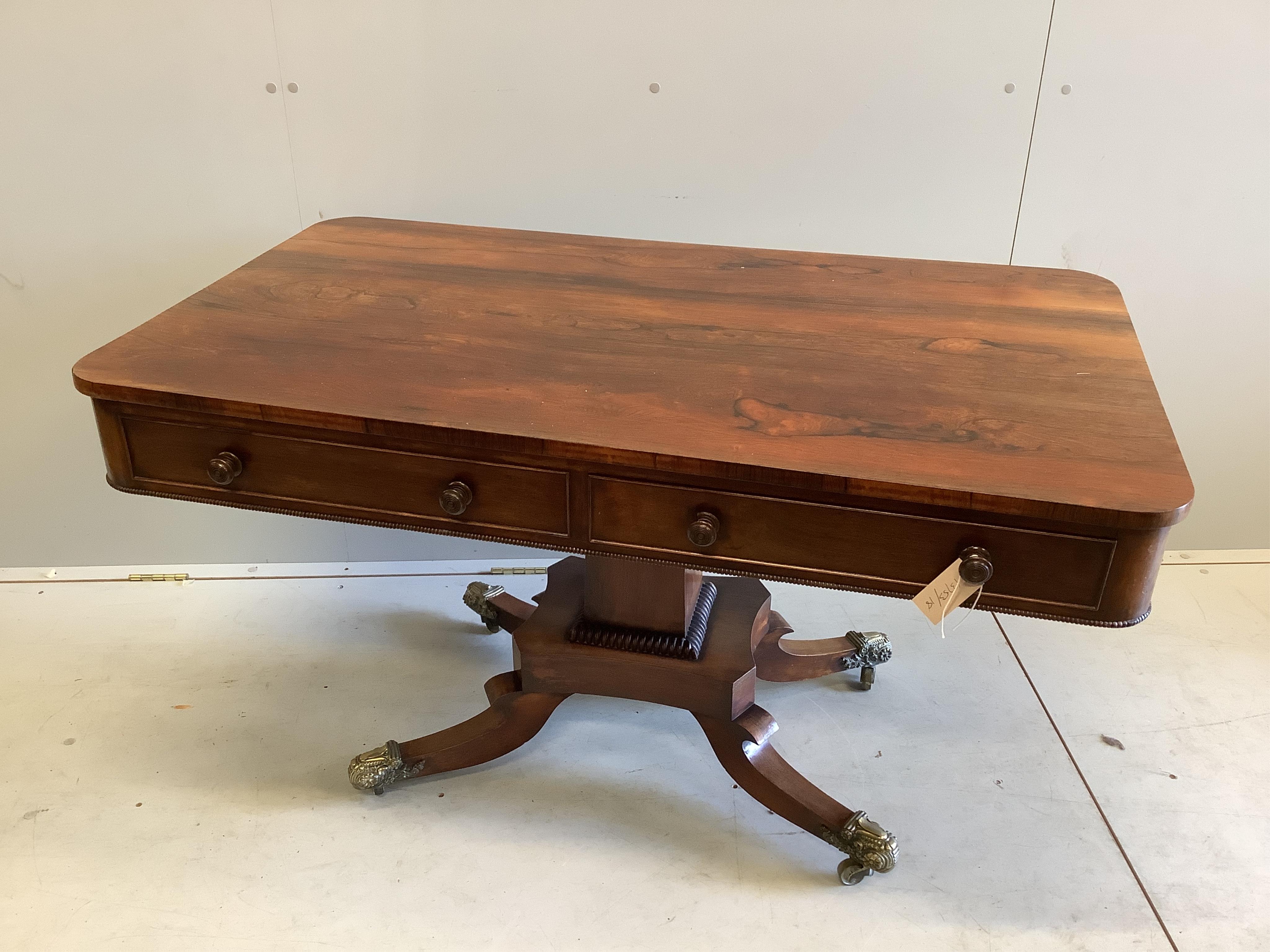 A Regency rectangular rosewood centre / library table, fitted two frieze drawers and two dummy drawers on single square tapered support, quadrapartite slab base and splayed legs with brass castors, width 123cm, depth 70c